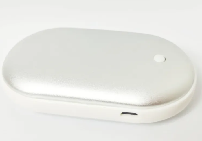AeroWarm rechargeable hand warmer in silver, pebble-shaped design with USB port for charging